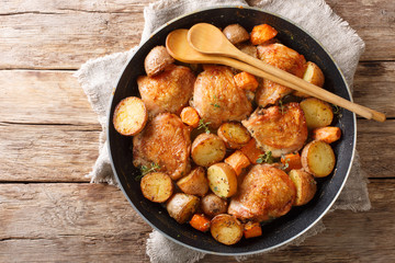 Cooked chicken thighs with potatoes and carrots close-up in a pan. Horizontal top view