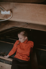 Slender blonde with pigtail in skirt sits in attic