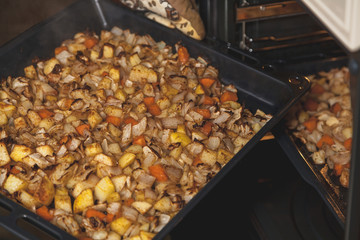Hands in mittens take out baking tray with vegetables oven