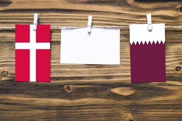 Hanging flags of Denmark and Qatar attached to rope with clothes pins with copy space on white note paper on wooden background.Diplomatic relations between countries.