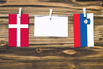 Hanging flags of Denmark and Slovenia attached to rope with clothes pins with copy space on white note paper on wooden background.Diplomatic relations between countries.