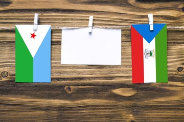 Hanging flags of Djibouti and Equatorial Guinea attached to rope with clothes pins with copy space on white note paper on wooden background.Diplomatic relations between countries.