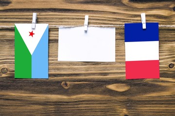 Hanging flags of Djibouti and France attached to rope with clothes pins with copy space on white note paper on wooden background.Diplomatic relations between countries.