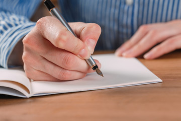 Beautiful Female hands write pen in a notebook of tasks and goals to work on a wooden table