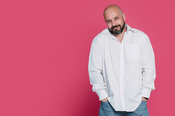 Fototapeta premium Handsome serious middle-aged man in a white shirt smiles on a pink background with copy space