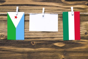 Hanging flags of Djibouti and Hungary attached to rope with clothes pins with copy space on white note paper on wooden background.Diplomatic relations between countries.