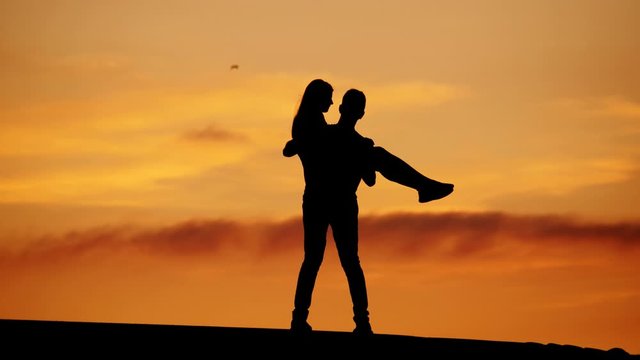 Woman jump on hands of man, happy couple turn around, black silhouette against yellow sky. Two people at top, celebrate some or just have fun, guy hold girl and rotate.