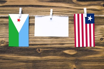 Hanging flags of Djibouti and Liberia attached to rope with clothes pins with copy space on white note paper on wooden background.Diplomatic relations between countries.