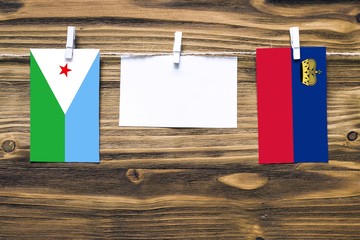 Hanging flags of Djibouti and Liechtenstein attached to rope with clothes pins with copy space on white note paper on wooden background.Diplomatic relations between countries.