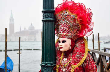 Fototapeta na wymiar Masked Venetian Performer on Wooden Pier by Gondola in Venice, Italy