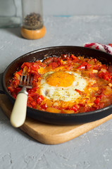Traditional Oriental dish of shakshuka eggs in a dark pan on a gray background .