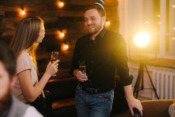 Young man and woman enjoying conversation in festively decorated house holding glasses of champagne in hand. Young couple talking on New Year Eve