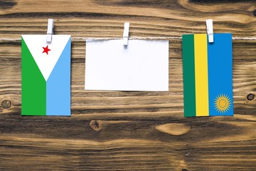 Hanging flags of Djibouti and Rwanda attached to rope with clothes pins with copy space on white note paper on wooden background.Diplomatic relations between countries.