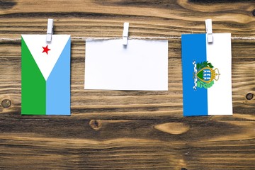 Hanging flags of Djibouti and San Marino attached to rope with clothes pins with copy space on...