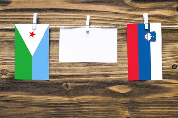 Hanging flags of Djibouti and Slovenia attached to rope with clothes pins with copy space on white...