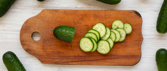 Ripe mini baby cucumbers on a rustic wooden board on a white wooden surface, top view. Flat lay, overhead, from above. Closeup.