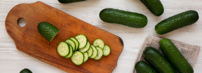 Fresh organic mini baby cucumbers on a rustic board on a white wooden surface, top view. Flat lay, from above, overhead.