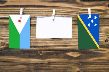 Hanging flags of Djibouti and Solomon Islands attached to rope with clothes pins with copy space on...