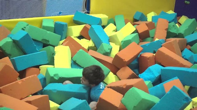 Cute funny shollboy plays with soft cubes in the dry pool. Kid playing on indoor playground in foam rubber pit in trampoline. Child having fun 