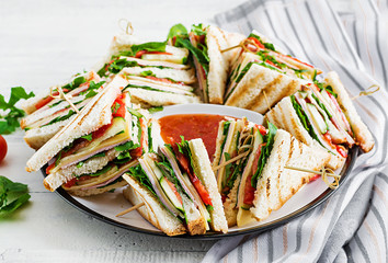 Club sandwich with ham, tomato, cucumber, cheese,  and arugula on wooden background.