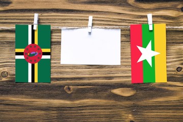 Hanging flags of Dominica and Myanmar attached to rope with clothes pins with copy space on white note paper on wooden background.Diplomatic relations between countries.