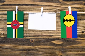 Hanging flags of Dominica and New Caledonia attached to rope with clothes pins with copy space on...