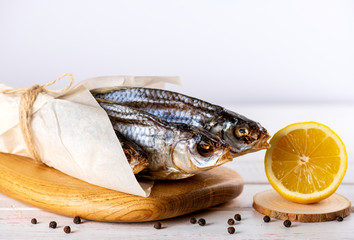 close up of dried and salted river fish on a wooden Board in white paper with lemon and pepper