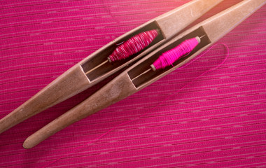Pink yarn in weaving shuttle tool on traditional handmade fabric. Textile weaving. Weaving using traditional weaving loom and shuttle.Textile production in Thailand. Asian culture. OTOP product.