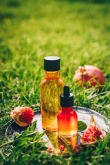 Trendy sunlight pomegranate seed oil, whey in different bottles on green grass background. Concept of anti-aging organic skin care.