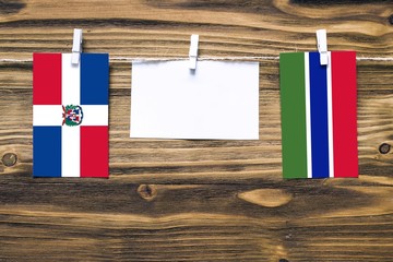 Hanging flags of Dominican Republic and Gambia attached to rope with clothes pins with copy space on white note paper on wooden background.Diplomatic relations between countries.