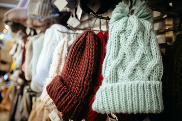Light blue burgundy knitted hats with pompoms on hangers selling in shop