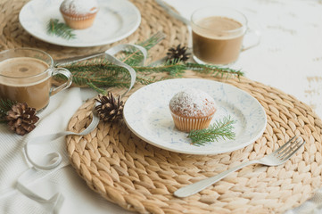 Christmas table setting with muffins, coffee, white plates, wicker coasters, fir branches and cones. Table setting in a rustic style for the New Year.