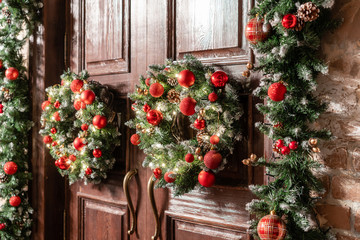 House entrance decorated for holidays. Christmas decoration. Two wreaths and garland of fir tree branches. Large wooden door