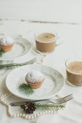 Christmas table setting with cupcakes, coffee, white plates, beads with pearls, spruce branches and cones. Table setting in a rustic style for the New Year.