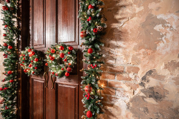 Fototapeta na wymiar House entrance decorated for holidays. Christmas decoration. Two wreaths and garland of fir tree branches. Large wooden door