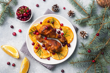 Baked chicken drumstick with oranges and cranberries in a plate light grey background. Christmas food Table with decorations.