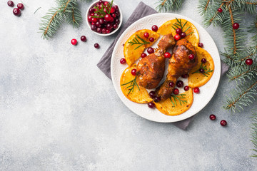 Fototapeta na wymiar Baked chicken drumstick with oranges and cranberries in a plate light grey background. Christmas food Table with decorations. Copy space.