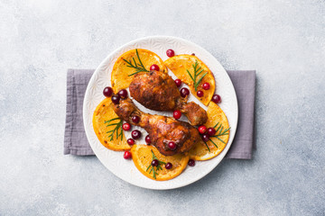 Baked chicken drumstick with oranges and cranberries in a plate light grey background. Christmas food Table with decorations. Copy space.