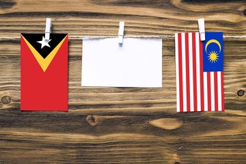 Hanging flags of East Timor and Malaysia attached to rope with clothes pins with copy space on white note paper on wooden background.Diplomatic relations between countries.