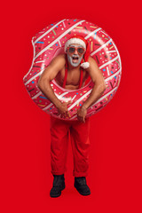 Handsome Santa Claus in sun glasses standing with inflatable ring for pool