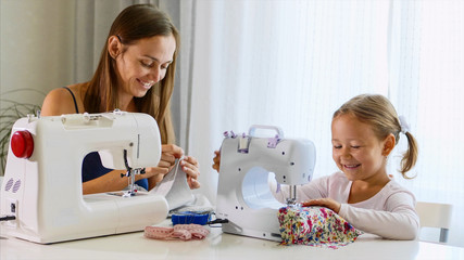 Mother and daughter is sewing on a machine. A woman using a needle. A mother and a daughter are...