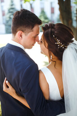 The bride and groom walk together in the park. Charming bride in a white dress, the groom is dressed in a dark elegant suit. Pretty bride and stylish groom. Wedding day. Marriage.