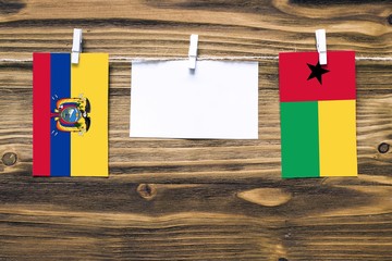 Hanging flags of Ecuador and Guinea Bissau attached to rope with clothes pins with copy space on white note paper on wooden background.Diplomatic relations between countries.