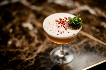 Cocktail in the glass decorated with a mint leaf branch, red peppercorns and dried orange slice