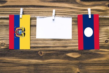 Hanging flags of Ecuador and Laos attached to rope with clothes pins with copy space on white note paper on wooden background.Diplomatic relations between countries.