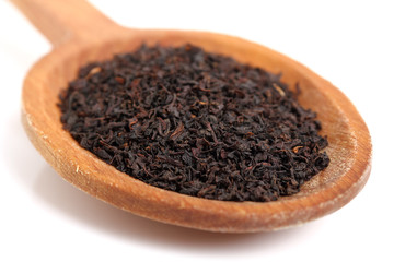 Loose dried black tea leaves on wooden spoon. Isolated on white background. Macro.