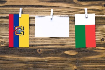 Hanging flags of Ecuador and Madagascar attached to rope with clothes pins with copy space on white note paper on wooden background.Diplomatic relations between countries.