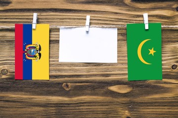 Hanging flags of Ecuador and Mauritania attached to rope with clothes pins with copy space on white note paper on wooden background.Diplomatic relations between countries.