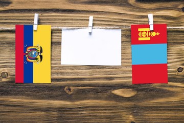 Hanging flags of Ecuador and Mongolia attached to rope with clothes pins with copy space on white note paper on wooden background.Diplomatic relations between countries.