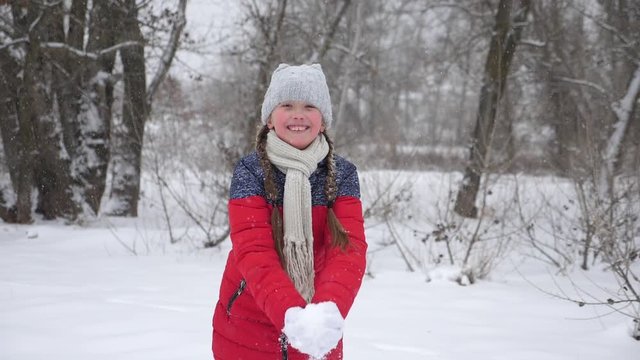 happy child girl throws snow with her hands in forest. Snow falls and sparkles in sun. child plays in winter in park for Christmas vacation.